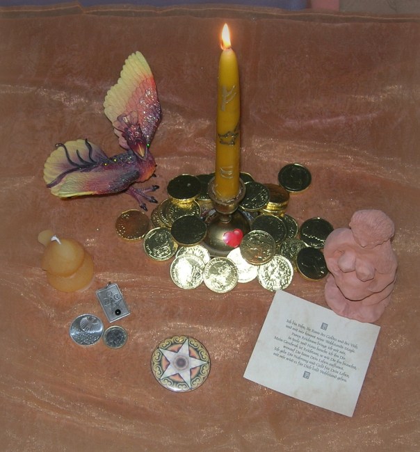 Von links nach rechts: Der Phönix, meine persönliche Beziehung zur Sternschnuppe, eine kleine Vogelkerze, symbolisch für die Zaunköniginnen, eine 10 € Münze, mit einem astronomischen Motiv - ein Geschenk an mich von einer Hexenschwester, eine maltesische 1 € Münze mit  Göttinnenidol, ein Button, der die Münzen des Tarot repräsentiert, die Geldkerze mit einer Sternschnuppe in der Mitte, umgeben von Goldmünzen, die mir Frau Holle einst für gute Dienste schenkte, eine Runenkarte 'Fehu' und eine handgefertigte Göttin, die ich bei einem Julfest von einer Mithexe geschenkt bekam.